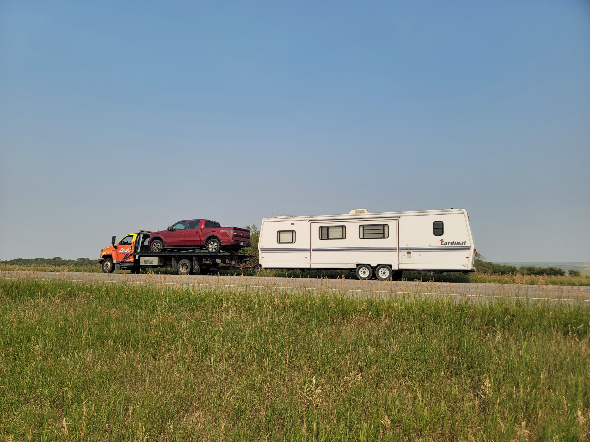 Flatbed towing a pickup while hauling a large RV trailer on Alberta highway