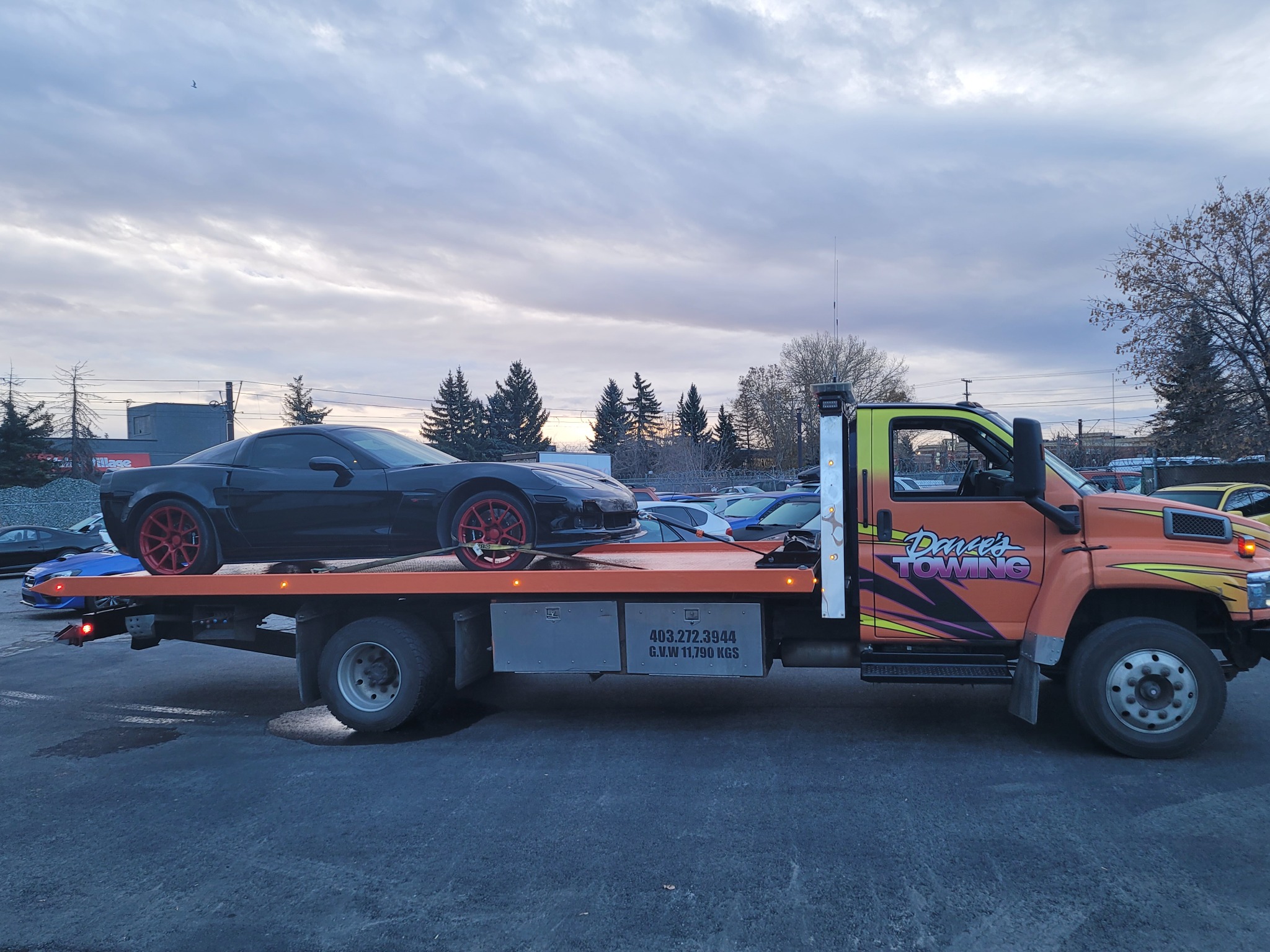Flatbed towing a black sports car with red wheels