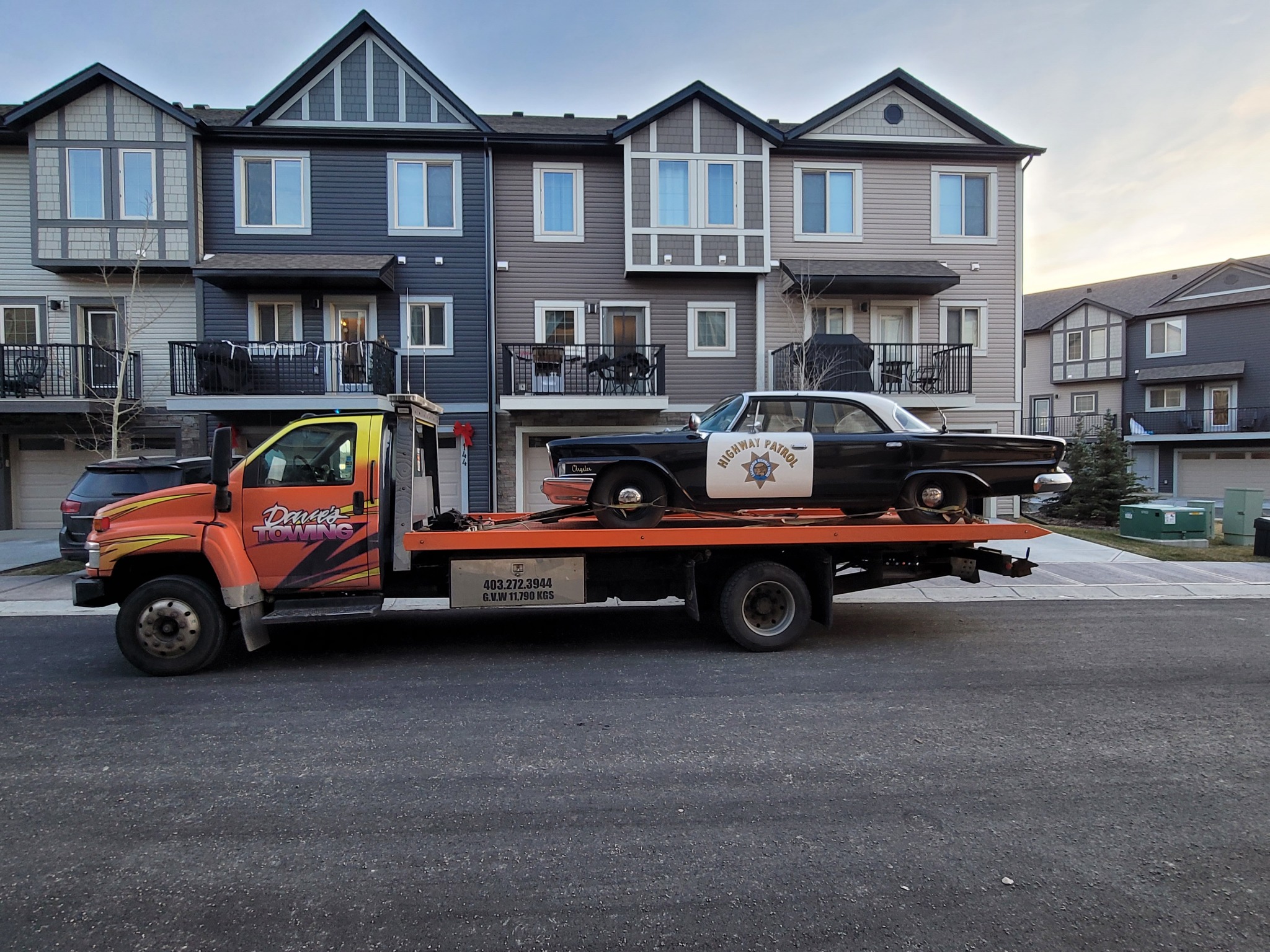 Flatbed transporting a classic Highway Patrol car in residential area