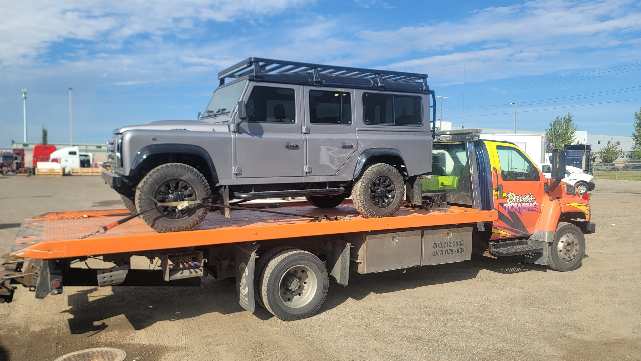 Flatbed transporting a Land Rover Defender at yard